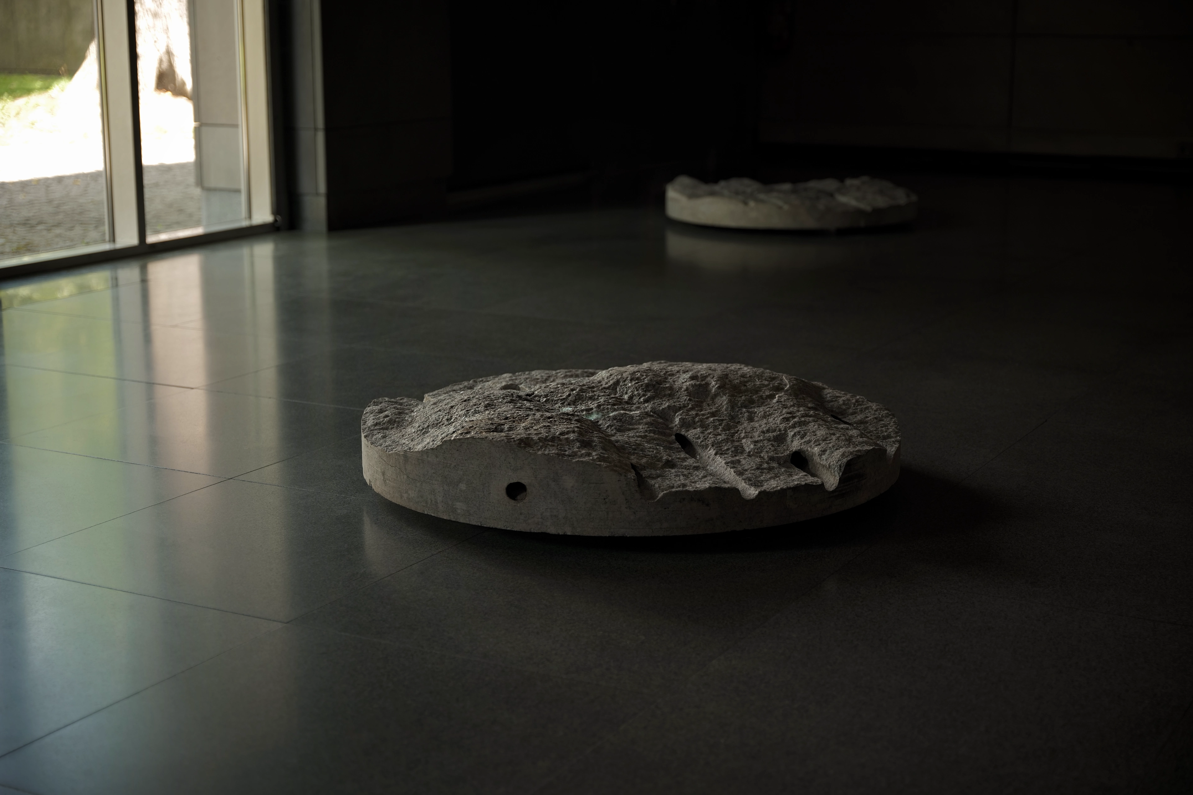 Granite sculptures from "Primes" by Ewa Wes Wesołowska, illuminated by moving projections of subatomic particle interactions.